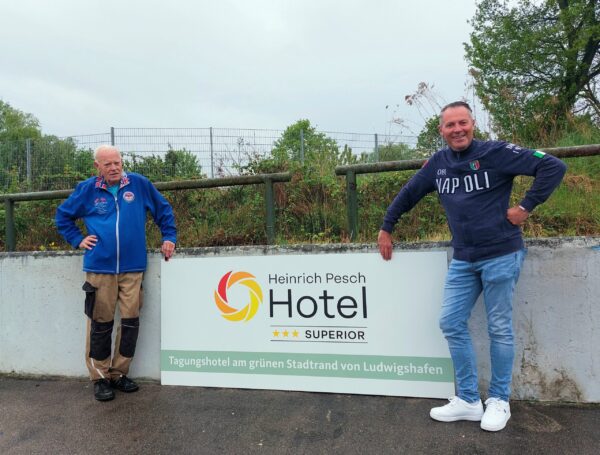 2 Männer neben einer Bande auf der Radrennbahn